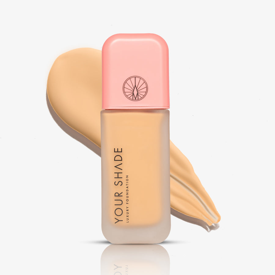 A bottle of luxury foundation by Your Shade, featuring a light pink cap and a frosted glass bottle showing the beige foundation liquid inside, set against a matching beige liquid swatch on a clean white background.