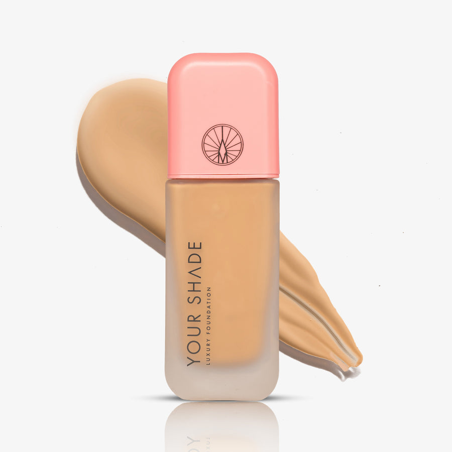 A bottle of Your Shade Liquid Foundation with a peach-colored cap, set against a beige makeup swatch on a clean white background.