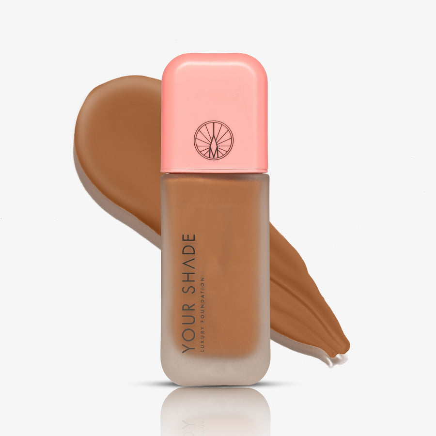 A bottle of liquid foundation with a pink cap and a warm tan-brown shade displayed behind it on a clean white background.