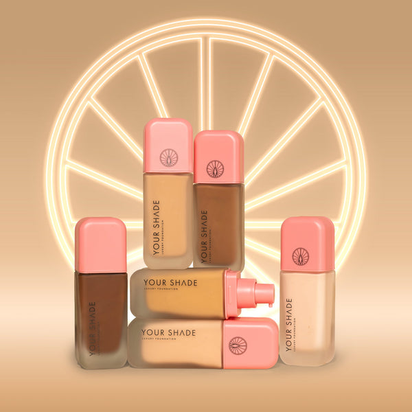 Four bottles of Armani Beauty Your Shade liquid foundation in various skin tones, arranged in front of a glowing circular wheel graphic on a warm beige background.